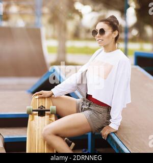 Junge Frau in Sonnenbrillen ruht im Park zum Skateboarden an einem sonnigen Sommermorgen. Stockfoto