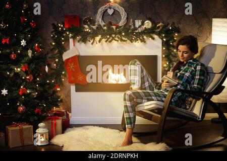 Glückliche Frau sitzt im Schaukelstuhl neben dem Kamin und Schreibt Plan für das nächste Jahr Stockfoto