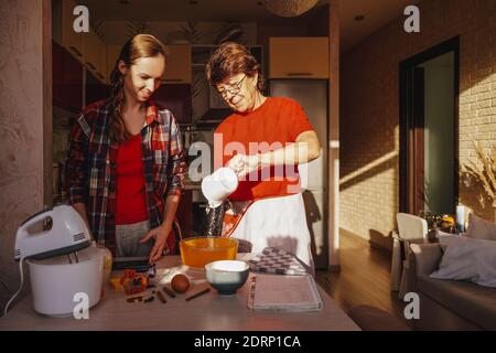 Junge Frau und ältere Mutter kochen Kekse in roten Kleidern. Stockfoto
