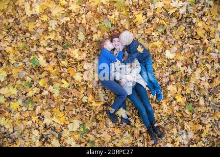 Mutter und zwei Kinder liegen in einem großen Stapel von Blättern. Söhne küssen Mama. Draufsicht Stockfoto