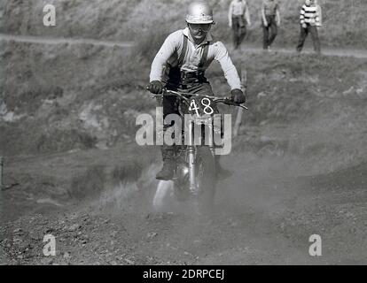 1970er Jahre, historisch, Motorcross... ein männlicher Fahrer, der einen Sturzhelm und eine Schutzbrille der damaligen Zeit trägt und einen kleinen Hügel hinauffährt, während er an einem Motorradrennen teilnimmt, England, Großbritannien. Stockfoto