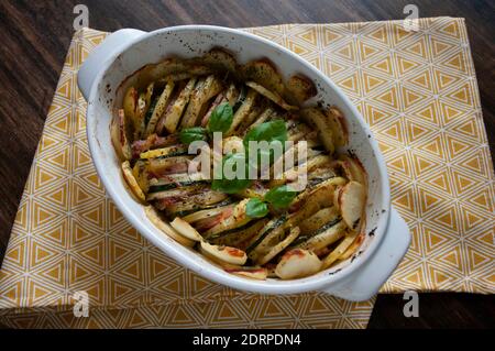 Herzhafte Kartoffelgratin Speck und Zucchini, frisch aus dem Ofen auf einem Holztisch serviert.Auflauf. Stockfoto