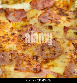 Nahaufnahme der leckeren hawaiianischen Pizza mit Käse, knusprigem Speck und Ananas auf Holzpizzabrett und weißem Hintergrund. Stockfoto