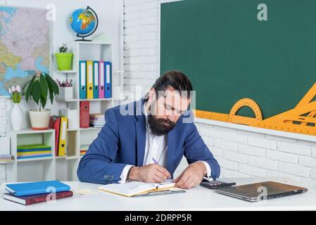 college-Dozent auf Lektion. Zurück zur Schule. Formale Bildung. Ernst reifen Lehrer Notizen in Planer. Brutal bärtigen Mann Arbeit im Klassenzimmer mit Notebook. Vorbereitung auf die Prüfung. Tür in die Zukunft. Stockfoto