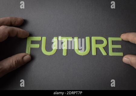 Menschliche Finger halten das Wort Zukunft geschrieben mit Plastikbuchstaben auf dunkelgrauem Papierhintergrund, Konzept Stockfoto