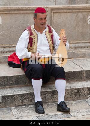 Dubrovnik, Dubrovnik-Neretva, Kroatien. Musiker in traditioneller Tracht spielt die dalmatinische dreisaitige lijerica neben dem Onofrio-Brunnen. Stockfoto