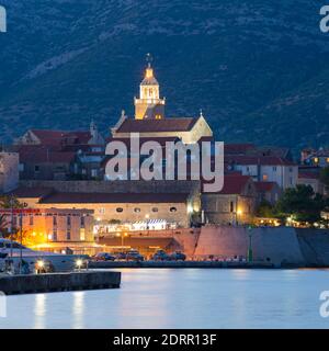 Korčula Stadt, Korčula, Dubrovnik-Neretva, Kroatien. Blick über den Jachthafen zur beleuchteten Altstadt, Dämmerung, Markusdom prominent. Stockfoto