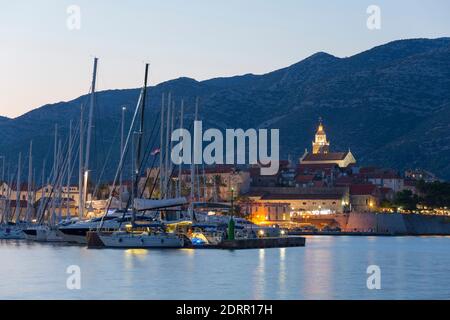 Korčula Stadt, Korčula, Dubrovnik-Neretva, Kroatien. Blick über den Jachthafen zur beleuchteten Altstadt, Dämmerung, Markusdom prominent. Stockfoto