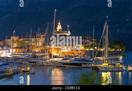 Korčula Stadt, Korčula, Dubrovnik-Neretva, Kroatien. Blick über den Jachthafen zur beleuchteten Altstadt, Dämmerung, Markusdom prominent. Stockfoto