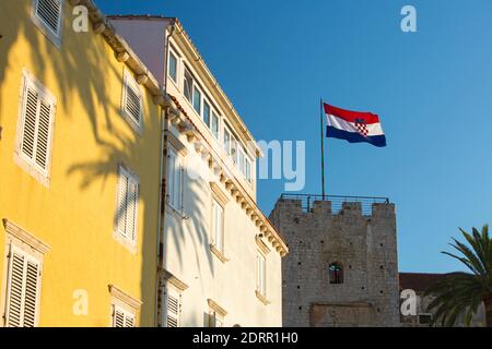 Korčula Stadt, Korčula, Dubrovnik-Neretva, Kroatien. Kroatische Flagge von der Spitze des Veliki Revelin Turms, bunte Häuser im Vordergrund. Stockfoto