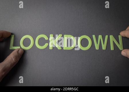 Menschliche Finger halten das Wort Lockdown geschrieben mit Plastikbuchstaben auf braunem Papier Hintergrund, Konzept Stockfoto