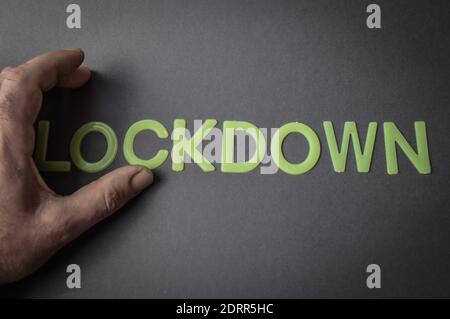 Menschliche Finger Entfernen des Wortes Lockdown geschrieben mit Plastikbuchstaben auf grauem Papierhintergrund, Konzept Stockfoto