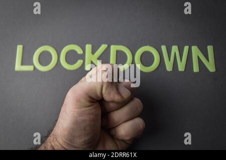 Menschliche Faust gegen das Wort Lockdown geschrieben mit Plastikbuchstaben auf grauem Papierhintergrund, Konzept Stockfoto