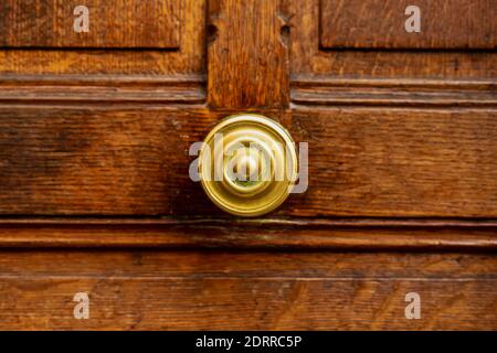 Alter runder Türgriff an alter brauner Holztür. Nahaufnahme Paris, Frankreich. Goldene Messingdetails an alter Holztür. Griff auf braunem altem Holz schäbig Stockfoto