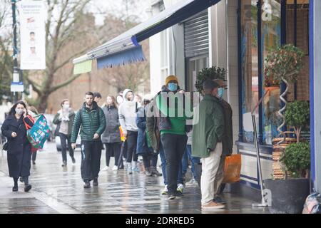 Clapham, London, 21. Dezember 2020: Im Regen stehen die Leute Schlange, um Weihnachtsaufträge von einem lokalen Metzger zu sammeln. Unter Tier 4 Coronavirus Einschränkungen sollten die Menschen zu Hause bleiben, außer für wesentliche Einkäufe und zur Arbeit zu gehen. Cafés und Restaurants sind nur für Essen zum Mitnehmen geöffnet und Deliveroo liefert Lebensmittel sowie warme Mahlzeiten. Anna Watson/Alamy Live News Stockfoto