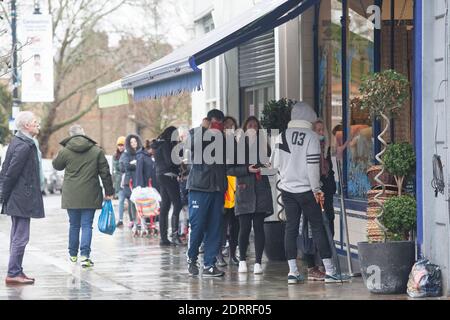 Clapham, London, 21. Dezember 2020: Im Regen stehen die Leute Schlange, um Weihnachtsaufträge von einem lokalen Metzger zu sammeln. Unter Tier 4 Coronavirus Einschränkungen sollten die Menschen zu Hause bleiben, außer für wesentliche Einkäufe und zur Arbeit zu gehen. Cafés und Restaurants sind nur für Essen zum Mitnehmen geöffnet und Deliveroo liefert Lebensmittel sowie warme Mahlzeiten. Anna Watson/Alamy Live News Stockfoto