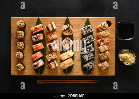Sushi-Set auf Holzbrett auf schwarzem Hintergrund serviert. Blick von oben. Flache Lay-Optik. Stockfoto