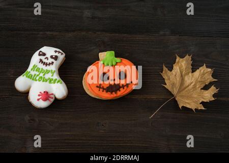 Lustige hausgemachte Halloween Kürbis und Geisterkekse auf Holzhintergrund neben Herbstblättern. Stockfoto