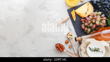 Rosenweinflasche Käsenüsse und rosa und schwarze Trauben, Honig. Camembert Käse, Weinbar Snacks. Weinzusammensetzung auf hellgrauem rustikalem Beton Stockfoto