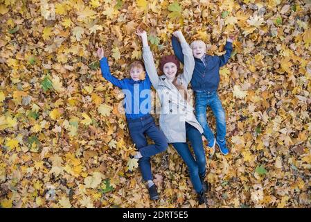 Glückliche Mutter und zwei Söhne liegen auf Herbstlaub im Wald. Draufsicht Stockfoto