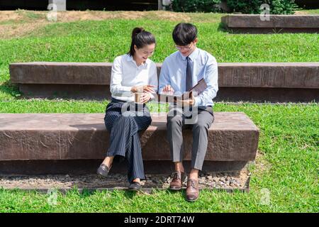 Zwei asiatische Business-Mitarbeiter außerhalb von Bürogebäuden diskutieren und kommentieren sich gegenseitig Arbeiten. Stockfoto