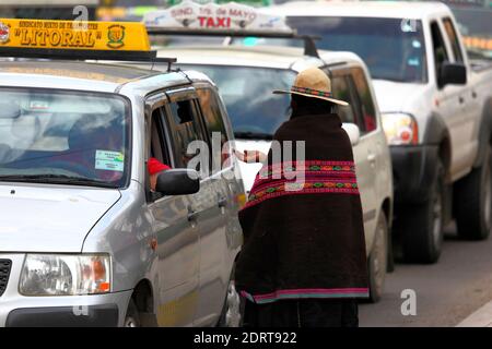 Quechua Frau aus dem nördlichen Potosi Department in traditioneller Kleidung betteln von Fahrern in der zentralen El Prado Straße, La Paz, Bolivien. Viele Frauen und Kinder kommen zur Weihnachtszeit aus dem nördlichen Potosi-Gebiet (einer der ärmsten in Bolivien) nach La Paz, um zu betteln, Geschenke zu erhalten und die allgemeine Solidarität der Bevölkerung zu fördern. Stockfoto