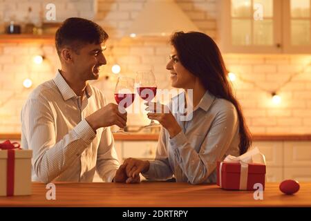 Lächelndes liebevolles Paar, das mit Gläsern Wein sitzt und die Hände während der Feier des Valentinstag hält Stockfoto