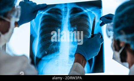 Nahaufnahme. Ärzte in Schutzkleidung diskutieren eine Röntgenaufnahme der Lunge . Stockfoto