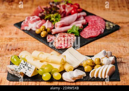 Wurstplatte und Käseplatte. Verschiedene Sorten Wurst und Käse mit Oliven auf einem schwarzen Teller auf einem Holztisch. Stockfoto