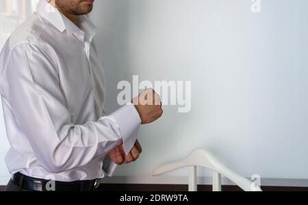 Ein Mann befestigt Manschettenknöpfe auf seinem weißen Hemd. Nahaufnahme der Hand eines Mannes, der ein weißes Hemd und Manschettenknöpfe trägt. Stockfoto