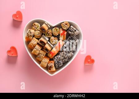 Sushi in Teller als Herz auf rosa Hintergrund gesetzt. Valentine Day Food Konzept. Blick von oben. Leerzeichen für Text. Flatlay-Style. Stockfoto