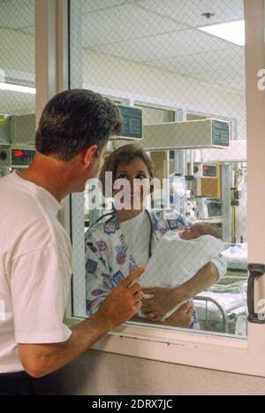 Stolzer Vater seinem neugeborenen Kind Thru Entbindungsstation Glas, 90er Jahre, USA Stockfoto