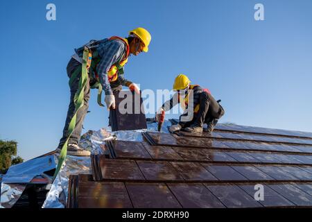 Zwei Bauarbeiter tragen einen Sicherheitsgurt Während der Arbeit und installieren Sie neue Keramik-Fliesendach mit Dachdecker Elektrowerkzeuge Stockfoto