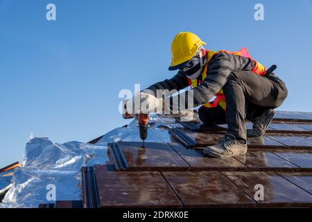 Bauarbeiter installieren neue keramische Fliesendach mit Dachwerkzeugen Elektrische Bohrmaschine in der Baustelle verwendet. Stockfoto