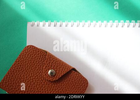 Leeres Notizbuch und braunes Leder-Portemonnaie auf grünem Tisch mit Fade-Ton, Platz für Text. Stockfoto