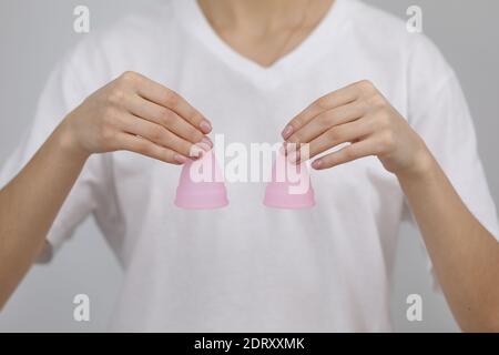 Nahaufnahme der Frau hält rosa Menstruationsbecher unterschiedlicher Größe in ihren Händen auf weißem Hintergrund. Konzept der Gynäkologie. Stockfoto