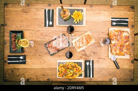 Zenith Blick auf rustikalen Tisch mit Nachos, traditionellen Schinken Pizza, Chips und Burger, Thunfisch Tataki und einen Teller mit Schinken Stockfoto