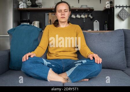Frau praktiziert Yoga oder meditiert zu Hause auf der Couch Stockfoto