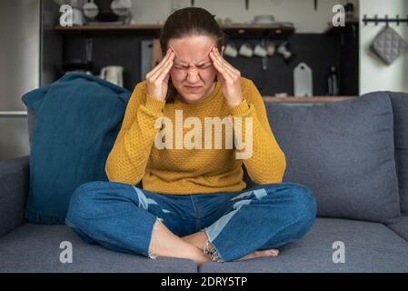 Frau mit Kopfschmerzen Kopf auf Couch in der Küche oder halten Wohnzimmer Stockfoto