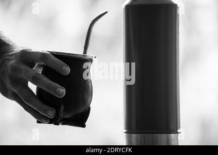 Grauskala selektiver Fokus Aufnahme einer Hand, die einen Kalabash hält Mate Becher mit Stroh Stockfoto