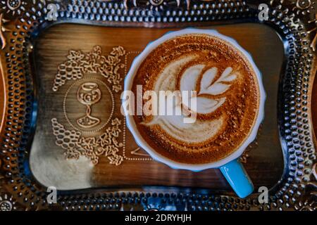 Eine große blaue Tasse mit Kaffee und einem Muster auf dem Schaum auf einem schönen Tablett in einem Café. Latte Art. Draufsicht Stockfoto