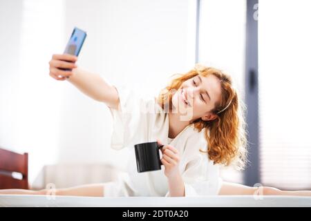 Casual sorglos Mädchen zu Hause mit Smartphone. Liegen im Bett Scrollen selbstmachen Fotos. Stockfoto