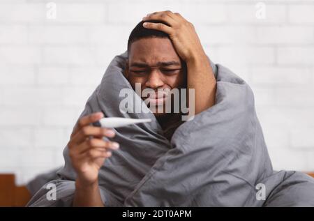 Kranker Afrikanischer Mann Mit Thermometer, Das Fieber Hat, Das Zu Hause Sitzt Stockfoto