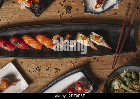 Ein Blick von oben auf eine Vielzahl von Sushi, Nigiri, Sashimi, Yakisoba und Edamame auf einem Restaurant Holztisch Stockfoto