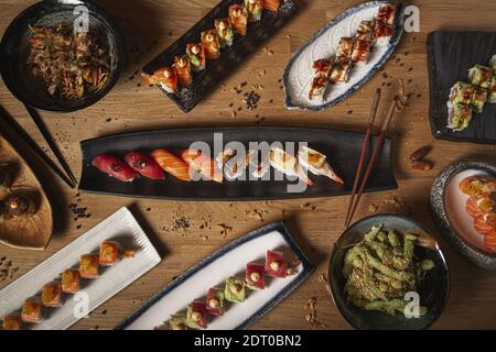 Ein Blick von oben auf eine Vielzahl von Sushi, Nigiri, Sashimi, Yakisoba und Edamame auf einem Restaurant Holztisch Stockfoto