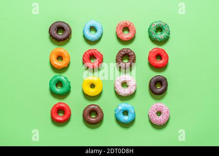 Draufsicht mit glasierten Donuts symmetrisch auf grünem Hintergrund ausgerichtet. Auswahl an bunten hausgemachten Schokoladendonuts. Stockfoto