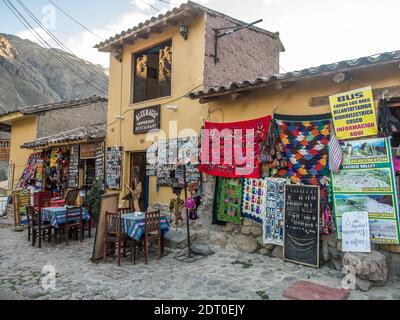 Ollantaytambo, Peru - 20. Mai 2016: Tische mit bunten peruanischen Tischdecken vor dem Restaurant auf der Straße in Ollantaytambo, Weg zum Eingang Stockfoto