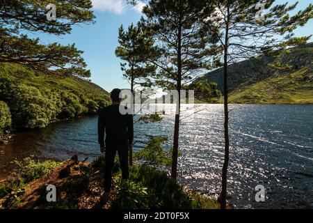 Junger Mann mit Blick auf Lough Veagh und die zerklüfteten Derryveagh Mountains mit blauem Himmel im Glenveagh National Park nordwestlich der Grafschaft Donegal, Irland Stockfoto