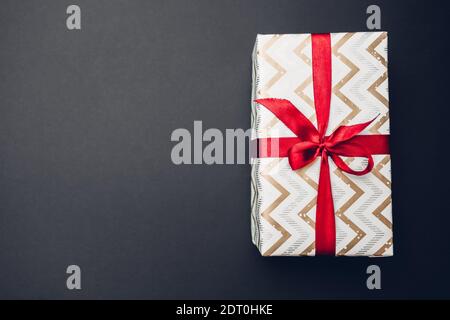 Weihnachts- und Neujahrsschachtel in Festpapier verpackt und mit rotem Band mit Schleife auf schwarzem Hintergrund verziert. Draufsicht. Platz Stockfoto