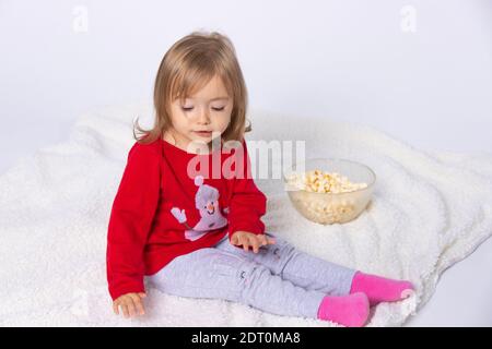 Kleines Kleinkind Mädchen sitzt auf einer flauschigen Decke mit Popcorn. Weißer Hintergrund. Stockfoto